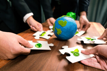 Cohesive group of business people holding eco icon jigsaw puzzle pieces around globe Earth as eco...