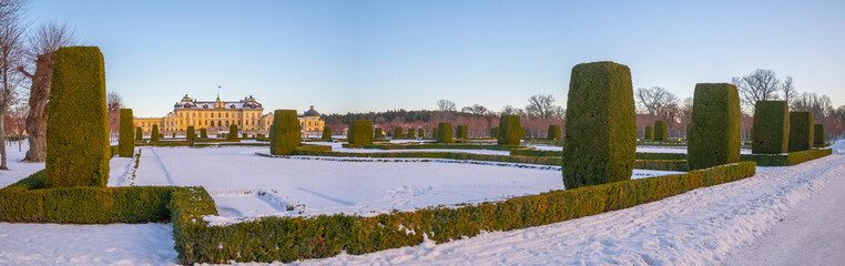 Panorama, snowy view over a winter garden and a castle in a park, on the Drottningholm island in Stockholm, Sweden