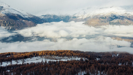 Aerial view of winter landscape with mountain peaks covered with snow, fluffy clouds and coniferous forest. Natural background.