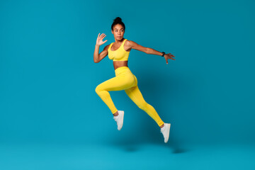 Fototapeta na wymiar Determined African American fitness woman jumps against blue studio background