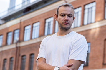 portrait of serious man standing against backdrop of an ancient red brick building. man in white...