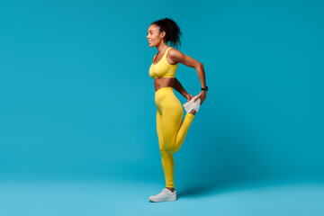 Black woman warming up stretching leg muscles over blue background