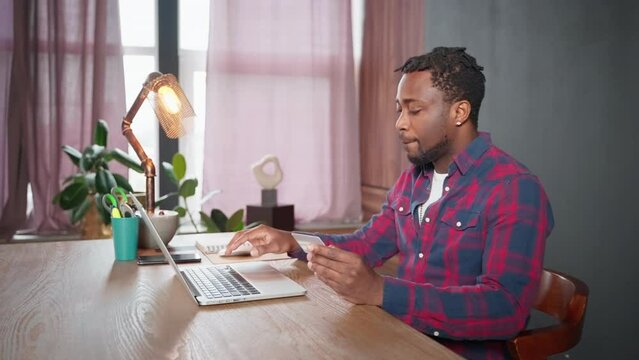 african businessman ordering and paying on website of internet-shop, sitting at table with laptop