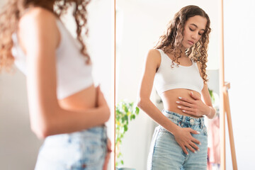 Teenager Girl Touching Stomach Standing Near Mirror At Home - obrazy, fototapety, plakaty