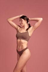 Happiness and wellness. Beautiful brunette young woman with slim healthy body standing in cozy cotton underwear over pink background. Concept of natural beauty, health and body care, body-positivity