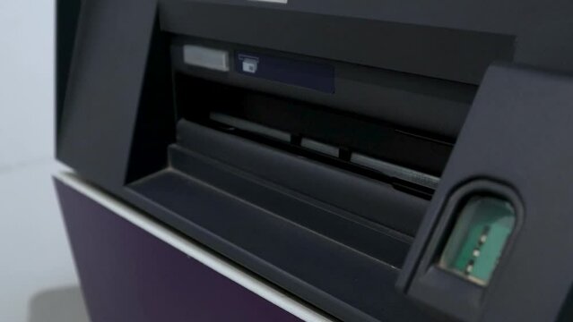 ATM machine dispensing Pak Rupee currency notes and an Asian man taking cash from the machine with his hand
