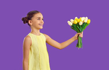 Happy kid with bouquet of spring flowers. Joyful child makes surprise for mum. Adorable little girl with cute hair buns isolated on purple background gives bunch of fresh tulips to mom on Mother's Day