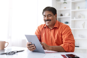 Fototapeta na wymiar Positive mature indian entrepreneur using digital tablet at home office