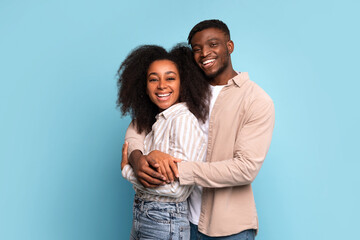 Affectionate african american couple embracing and smiling on blue background.