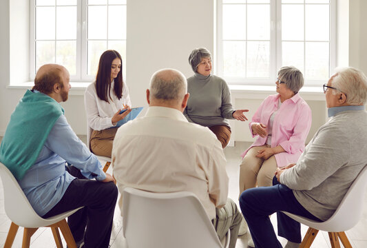 Old people communicating at group therapy meeting. Several male and female senior citizens sharing and talking about their concerns and problems at training workshop seminar with coach therapist
