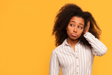 Pensive young black woman with hand on head looking aside on yellow background
