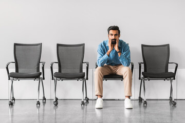 Anxious indian man seated alone with hands on face in waiting area