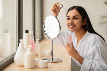 Attractive millennial indian woman applying serum on face