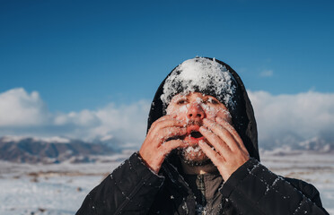 Young man touching his face with snow on mountains background in winter