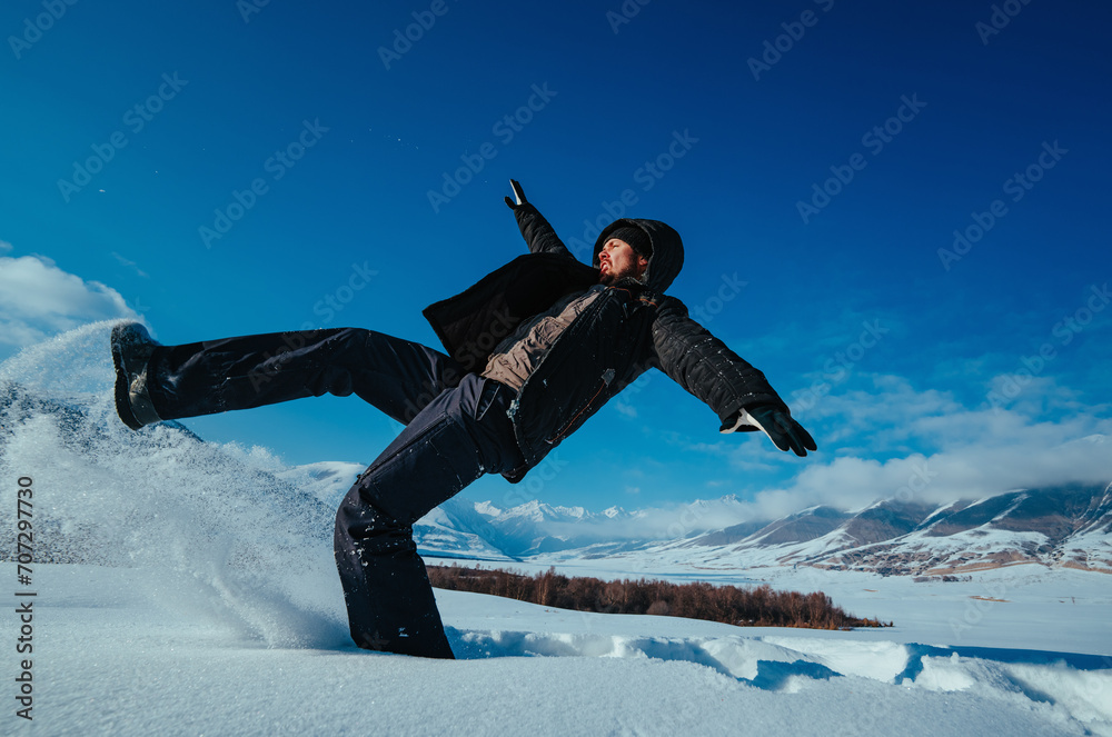 Wall mural Emotional young man falling in snow on mountains background in winter