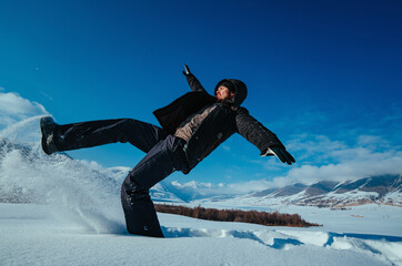 Emotional young man falling in snow on mountains background in winter