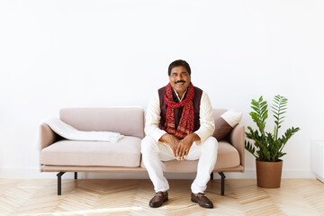 Positive mature indian man sitting on couch in living room