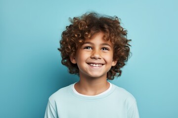 Cheerful little boy with curly hair looking at camera over blue background
