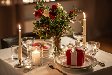 holidays, romantic date and celebration concept - close up of festive table serving for two with gift box, flowers in vase and candles burning at home on valentine's day