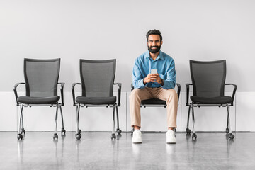 Smiling indian man with phone in hand sitting in an empty waiting room