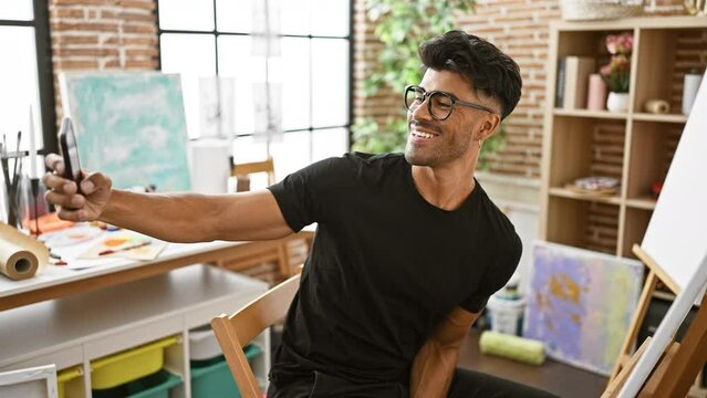 Handsome young latin man with beard smiles holding smartphone in creative indoor studio