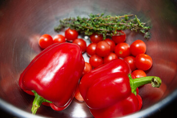 Fresh Red Bell Peppers and Cherry Tomatoes in Bowl. Shiny red bell peppers and ripe cherry tomatoes with a sprig of thyme in a metallic bowl, ingredients for a healthy dish.