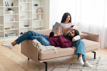 Cheerful eastern man and woman with gadgets chilling at home