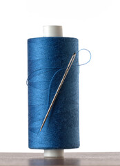 A spool of blue thread with a needle on a white background