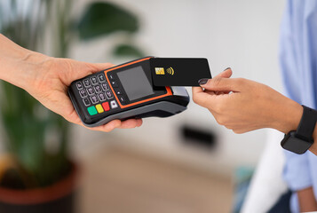 Hands of lady hold black contactless credit card over card reader to complete payment