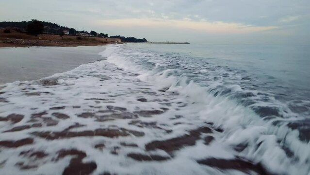 Drone soars low over beach at sunset, revealing vibrant sea, surf. Mesmerizing views of sea, surf. Stunning sea, surf, waves breaking along shoreline.