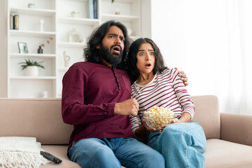 Shocked millennial indian couple watching horror movie on TV - obrazy, fototapety, plakaty