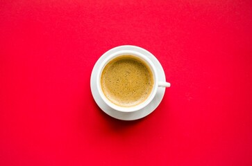 Cup of coffee close-up on a red background.  Flat lay top view, white cup with cappuccino stands on a white saucer, space for copy text.