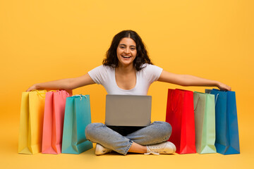 Young indian woman shopaholic using laptop, yellow background