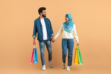 Muslim couple enjoying shopping together, holding hands and carrying colorful bags