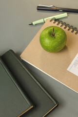 Green apple among educational supplies, active learning atmosphere. Books, fountain pens and notepad