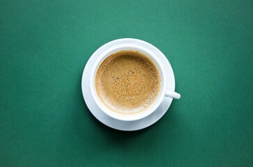 Cup of coffee close-up on a green background.  Delicate, tasty, aromatic cappuccino in a white cup on a white saucer, space for copy text, flat lay, top view.