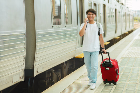 Chinese guy tourist walking by train station, talking on phone