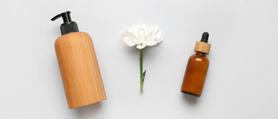 Bottles of cosmetic products and chamomile flower on light background