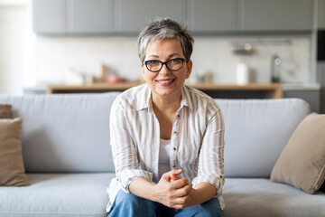 Smiling elderly woman sitting on couch in living room interior