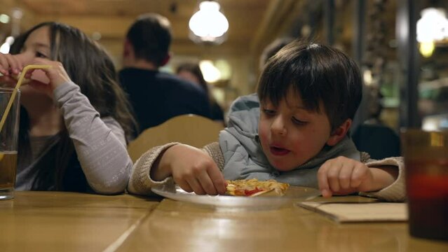 Small boy eating slice of pizza at restaurant, Child enjoying carb food nutrition at diner in the evening
