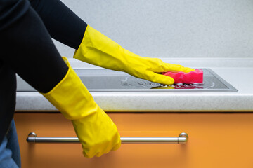 woman washing the hob in the kitchen wearing yellow gloves.