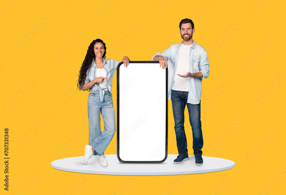 Poster man and woman presenting large smartphone display on yellow background