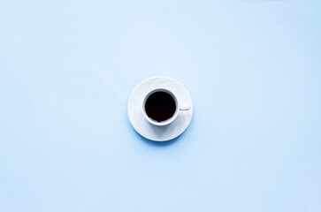 Cup of coffee on a blue background.  Delicate, tasty, aromatic black coffee in a small white cup on a white saucer, space for copy text, flat lay, top view.
