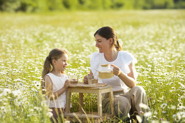 Lifestyle photo of beautiful family on picnic with chamomile healthy tea in nature landscape....