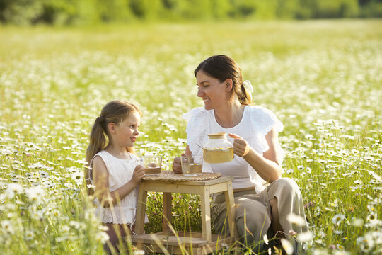 Lifestyle photo of beautiful family on picnic with chamomile healthy tea in nature landscape. Lovely mother with daughter sitting in daisy blooming field and spend time together. Happy mothers day.