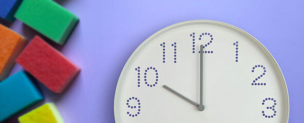 10 o'clock, morning. Cleaning time. Banner. White wall clock on background of multi-colored kitchen sponges. Time on clock is 10 am. Cleaning service and spring organizing concept.