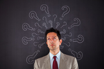 a man with a suit and tie is looking up at a blackboard with question marks on it