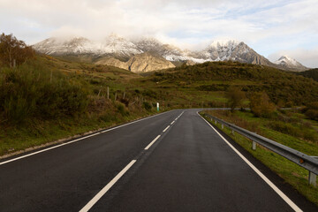 Landscape of road through Las Ubinas natural park with snowy mountains and autumn trees next to green meadow