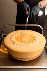 Chef melts cheese using a hand-held gas burner, head of Parmesan cheese, serving food in cheese