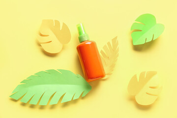 Bottle of sunscreen cream with paper palm leaves on yellow background